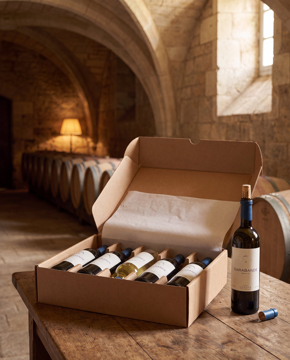 Open six-bottle shipping box with red and white wine bottles in the vaulted cellar of the Domaine aux Conseillans